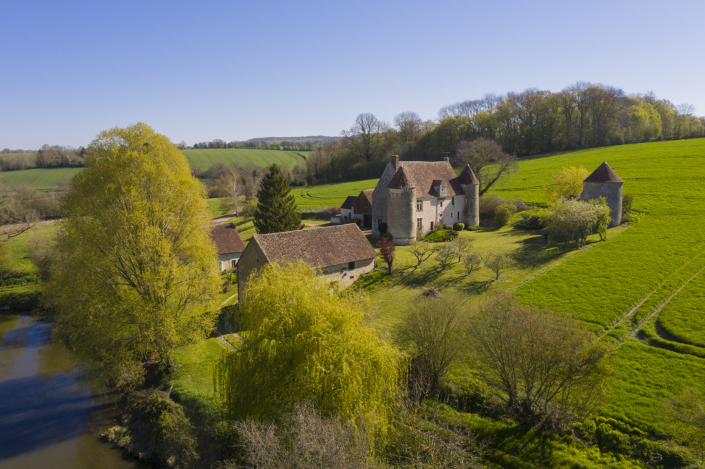 Le manoir de la Manorière à Vichères. Accrochée à mi-pente d’un coteau, la Manorière domine la vallée de la Berthe, petit affluent de l’Huisne, assez fortement encaissée pour la région, à l’approche de Vichères.Le manoir et ses communs descendent en pente douce vers trois étangs de belle taille, peut-être la survivance d’anciens viviers qui servaient de réserve à poissons.Le manoir est une ancienne maison forte. Ses deux tours d’angle sont chacune défendue par une bretêche et des meurtrières. Une autre bretêche veille de haut sur la porte d’entrée. Une troisième tour enfin, détachée du manoir, abrite un fournil en rez-de-chaussée et un pigeonnier au-dessus.Dès le milieu du XVIIe siècle, le manoir est laissé par ses propriétaires au fermier. Les cultures, aujourd’hui, lèchent pratiquement ses murs. Le bocage d’autrefois a cédé la place à deux immenses parcelles. L’une au-dessus des étangs, l’autre qui enserre littéralement la Manorière. Photographie extraite du projet photographique "les manoirs du Perche"