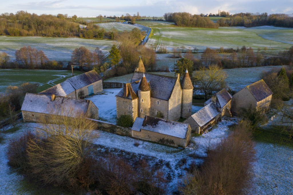 Le manoir de Lormarin à Nocé. Trapu, bien assis entre ses trois tours, entouré sur trois côtés par les bâti- ments des communs, Lormarin en impose au milieu de ce coteau qui descend lentement vers la Martinière, petit affluent de l’Erre, à deux pas de Nocé. C’est une maison relativement récente, érigée à la fin du XVIe siècle par un hobereau protestant. Il se construit alors sur un plan carré un manoir de cé- libataire, deux pièces l’une sur l’autre et deux tours. La tour d’escalier à l’ar- rière et la grosse tour de guet à l’avant. Le mariage du propriétaire, dix ans plus tard, l’amènera à doubler la superficie du manoir qui de carré deviendra rectangle avec l’adjonction d’une troisième tour en façade. Un siècle plus tard, la révocation de l’Édit de Nantes mettra un coup d’arrêt définitif aux travaux d’agrandissement poursuivis par les héritiers du premier bâtisseur.Lormarin a gardé de ses origines cette modestie rurale dans les extérieurs. Un potager, des arbres fruitiers, une cour en herbe jusqu’au pied des murs. Les propriétaires actuels ont reboisé les abords immédiats, totalement nus lorsqu’ils sont arrivés il y a vingt-cinq ans. Hélas, ils n’ont rien pu faire pour les six cents pommiers présents dans les champs alentour et qui ont disparu, victimes de la mécanisation et du remembrement. Photographie extraite du projet photographique "les manoirs du Perche"