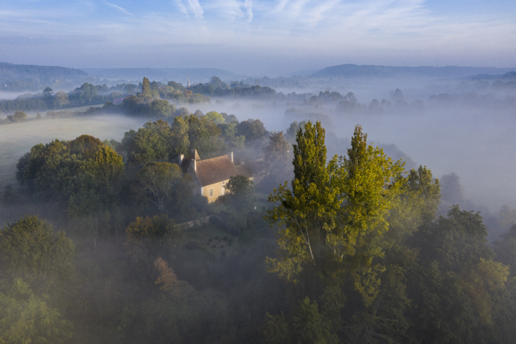 Le manoir de Pontgirard à Monceaux au Perche. Le Pontgirard émerge de la brume dans un paysage de collines boisées archétypal du Perche. C’est pratiquement au pied de la colline sur le flanc de laquelle il est édifié que la petite rivière la Jambée vient se jeter dans la Commeauche qui quelques kilomètres plus loin rejoindra l’Huisne.Le Pontgirard n’est pas une ancienne seigneurerie comme les autres manoirs. C’est à l’origine une « maison des champs » que des maîtres de forge fortunés se font construire au milieu du XVIe siècle.Le logis, modeste, se développe selon un plan en T avec, à l’arrière, une impressionnante toiture. Au début du XVIIIe siècle il fut modernisé à la recherche de confort, avec la construction du perron et l’agrandissement des ouvertures. Quelques décennies plus tard le logis cesse d’être habité régulièrement pour n’être plus qu’une ferme et il commence à se dégrader. Il sera racheté en 1969 par Philippe Siguret, grand spécialiste des manoirs du Perche, qui le restaurera dans les règles de l’art. Photographie extraite du projet photographique "les manoirs du Perche"